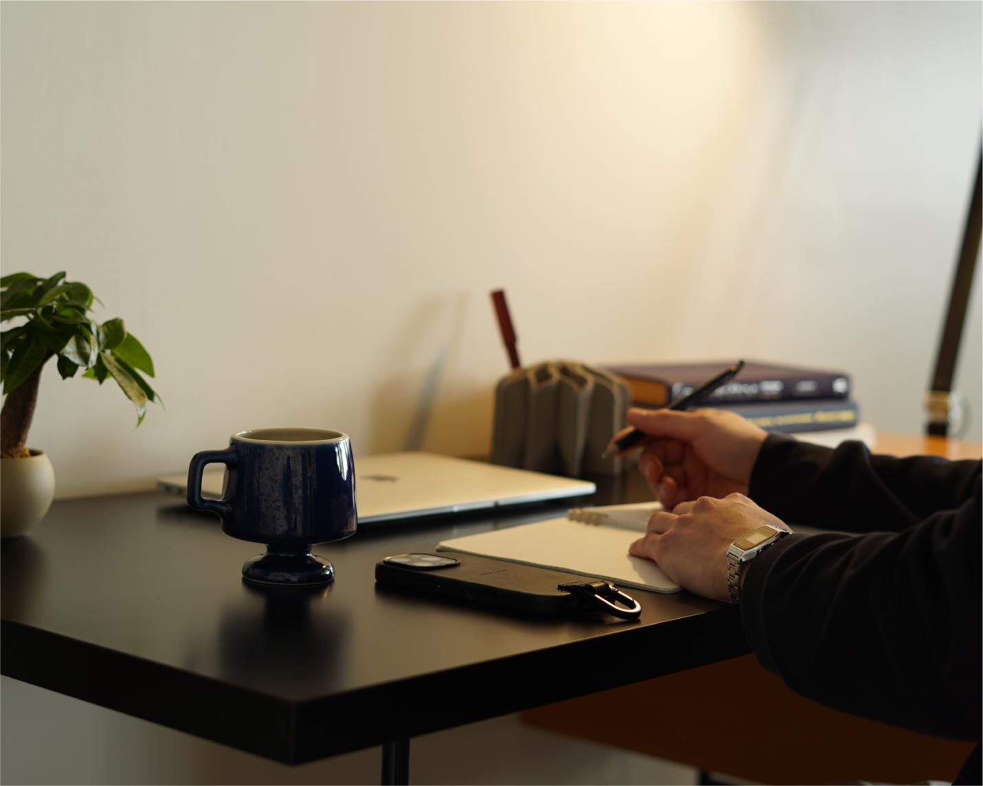 ゴブレットマグとデスクで書き物をする男性の手元